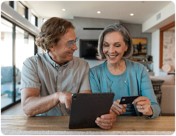 a man and a woman smiling and looking at a tablet while the woman reads off a credit card